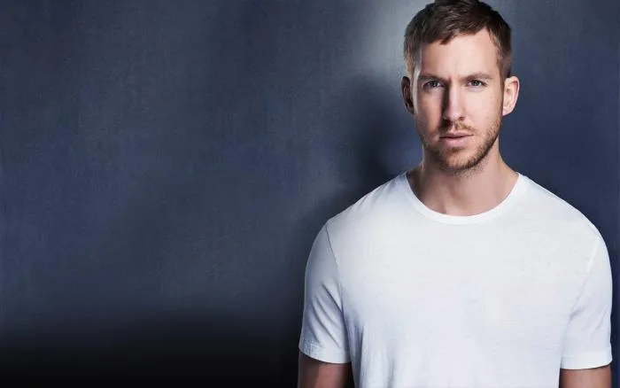Ο Calvin Harris ποζάρει με λευκό t-shirt σε σκούρο φόντο.