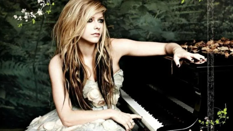 Η Avril Lavigne κάθεται δίπλα σε ένα μαύρο πιάνο σε δασικό σκηνικό.
