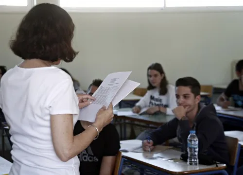 Καθηγήτρια σε τάξη λυκείου κρατάει έγγραφα μπροστά σε μαθητές.