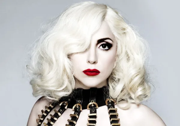 Κοντινό πορτρέτο της Lady Gaga με πλατινέ μαλλιά, κόκκινο κραγιόν και μαύρο ένδυμα με χρυσές λεπτομέρειες.