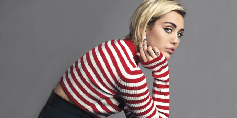 Η Miley Cyrus με ριγέ μπλούζα σε γκρι φόντο.