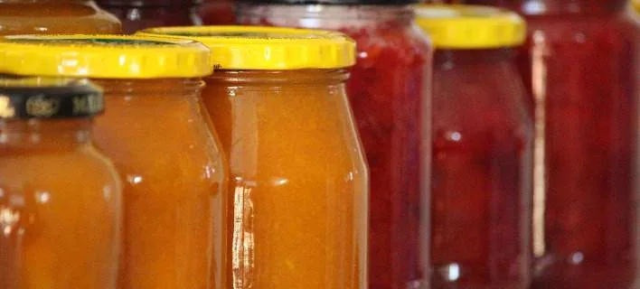 Σειρά από γυάλινα βάζα με μαρμελάδες σε διάφορα χρώματα.