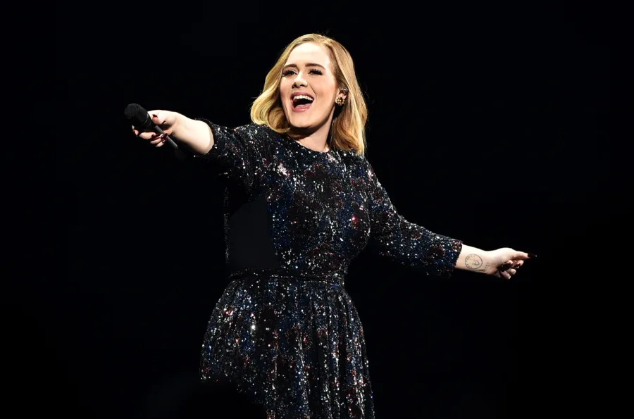 Η Adele τραγουδάει στη σκηνή φορώντας ένα αστραφτερό μαύρο φόρεμα.