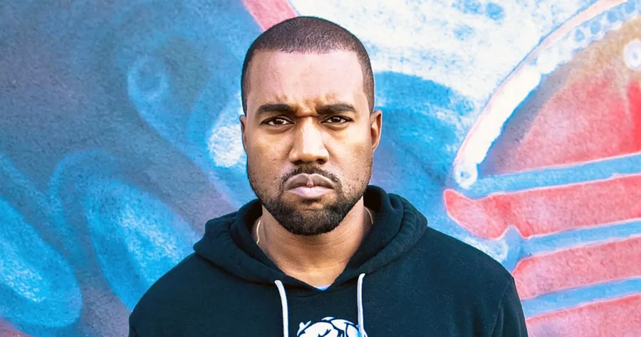 Ο Kanye West με μαύρο φούτερ μπροστά από γκράφιτι τοίχο.