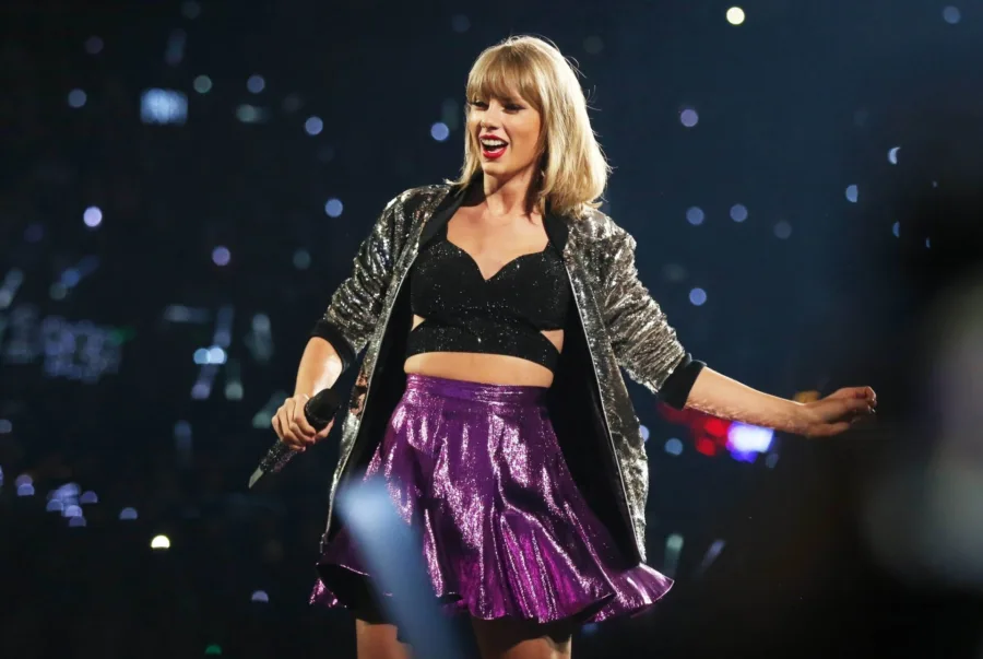 Η Taylor Swift στη σκηνή με αστραφτερό σακάκι και μωβ φούστα.