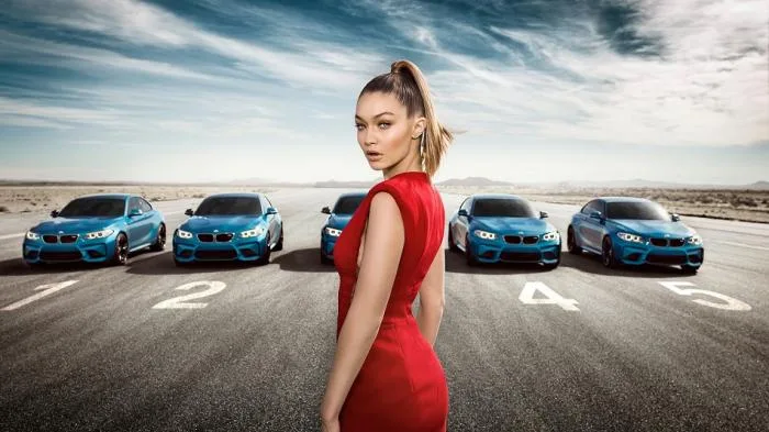 Η Gigi Hadid με κόκκινο φόρεμα μπροστά από πέντε μπλε αυτοκίνητα BMW.