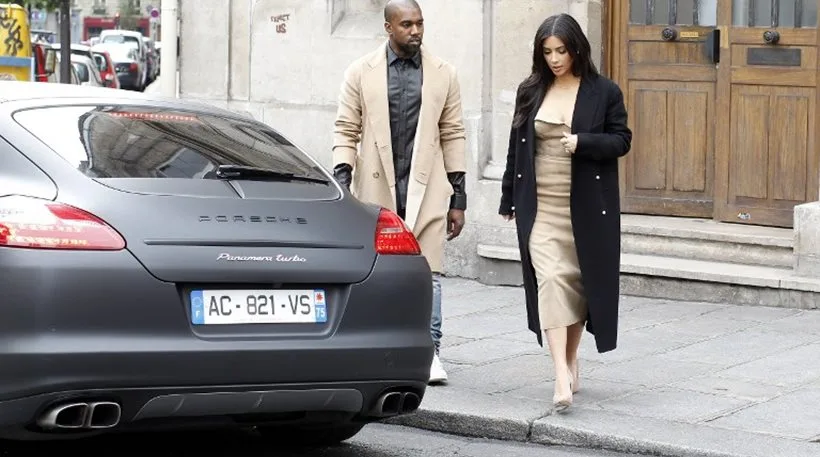 Η Kim Kardashian και ο Kanye West περπατούν στο Παρίσι δίπλα σε μια μαύρη Porsche Panamera.