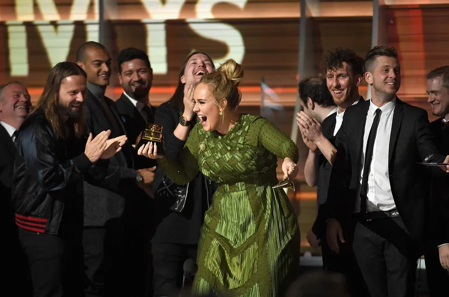 Η Adele πανηγυρίζει στη σκηνή των Grammys κρατώντας το βραβείο της.