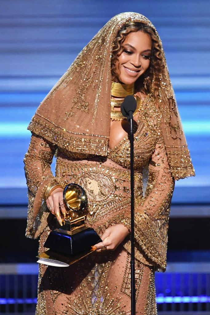 Η Beyoncé στα βραβεία Grammy με χρυσό φόρεμα και πέπλο, κρατώντας το βραβείο της.
