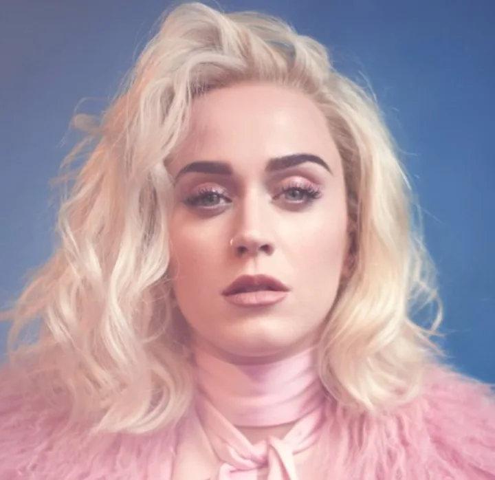 Η Katy Perry με ξανθά κυματιστά μαλλιά και ροζ ρούχα σε μπλε φόντο.