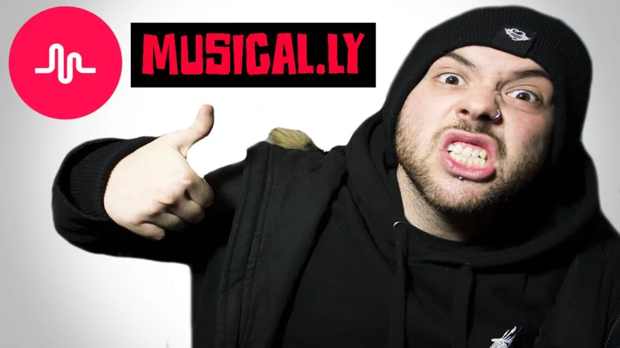 Ο YouTuber Noz με μαύρο σκούφο και φούτερ δείχνει το σήμα του Musical.ly.