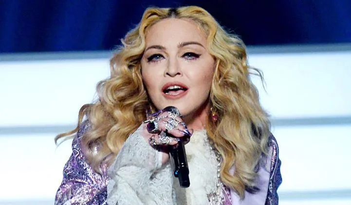 Η Madonna τραγουδάει σε σκηνή κρατώντας μικρόφωνο.