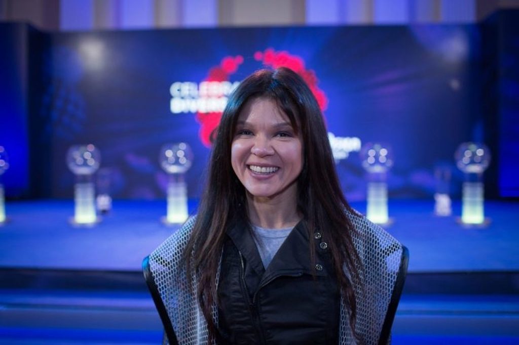 Η Ruslana χαμογελάει μπροστά από ένα μπλε σκηνικό.