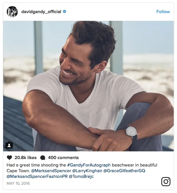Ο David Gandy χαμογελάει φορώντας λευκό t-shirt σε παραλία.