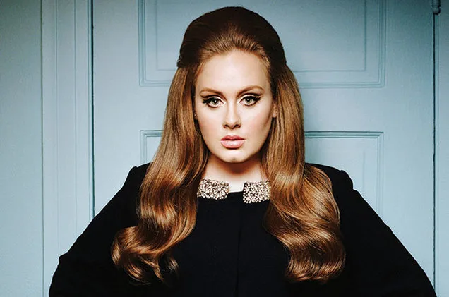 Η Adele με vintage χτένισμα και μαύρο ένδυμα μπροστά από γαλάζια πόρτα.