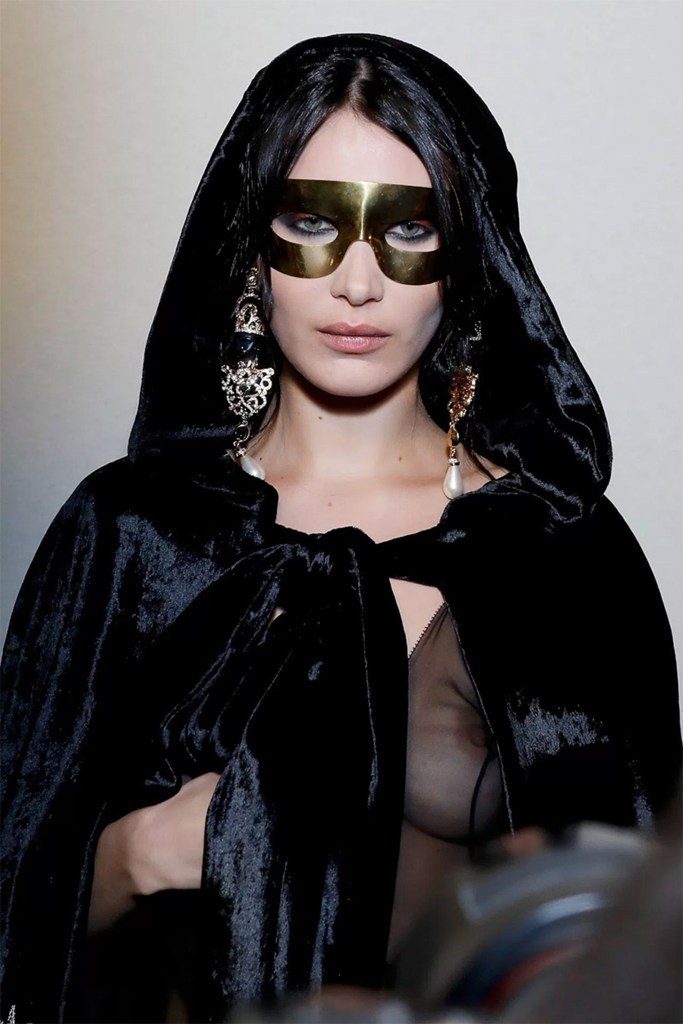 Η Bella Hadid με μαύρη βελούδινη κάπα και χρυσή μάσκα στην πασαρέλα.
