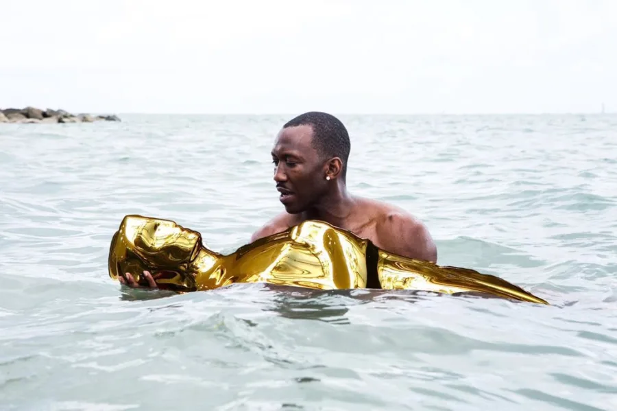Ο Mahershala Ali μέσα στη θάλασσα κρατώντας ένα χρυσό αγαλματίδιο Όσκαρ.