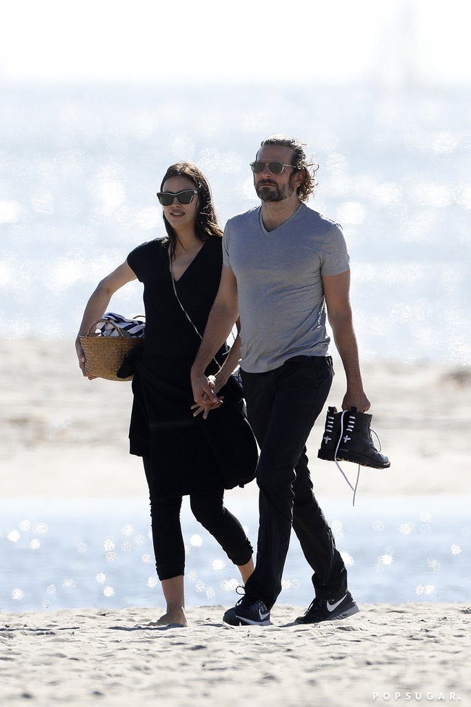 Η Irina Shayk και ο Bradley Cooper περπατούν χέρι-χέρι σε παραλία.