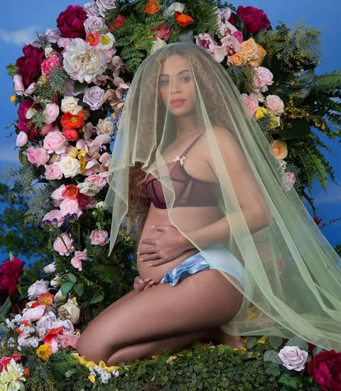 Η Beyoncé ποζάρει έγκυος μπροστά από μια αψίδα λουλουδιών.