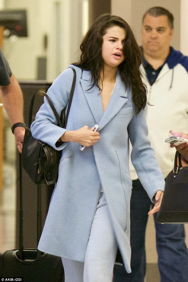 Η Selena Gomez με γαλάζιο παλτό και μαύρη τσάντα.