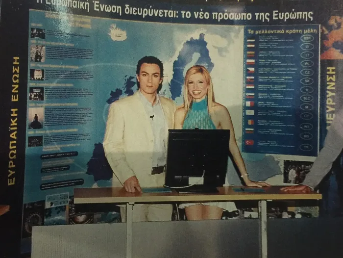 Ο Σάκης Τανιμανίδης και μια παρουσιάστρια σε τηλεοπτικό πλατό με χάρτη της Ευρωπαϊκής Ένωσης.