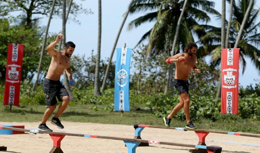 Δύο άνδρες παίκτες του Survivor σε αγώνισμα ισορροπίας σε παραλία.