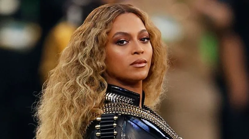 Η Beyonce με ξανθά κυματιστά μαλλιά και μαύρο δερμάτινο ένδυμα με χρυσές λεπτομέρειες.