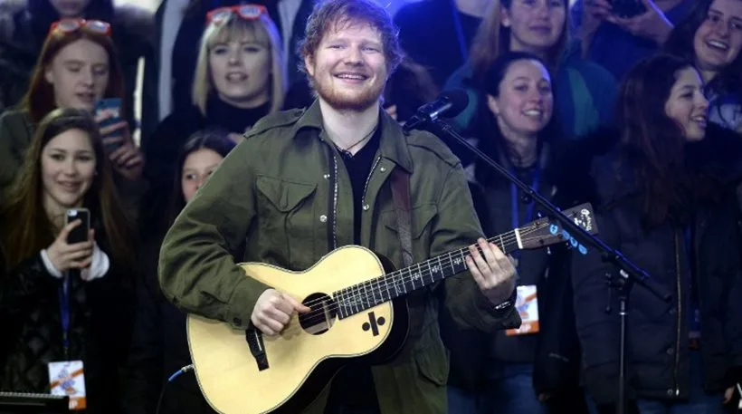 Ο Ed Sheeran παίζει ακουστική κιθάρα και τραγουδάει μπροστά σε κοινό.