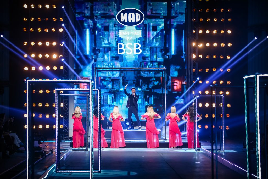 Καλλιτέχνης στη σκηνή του MadWalk 2017 με χορεύτριες στα κόκκινα.
