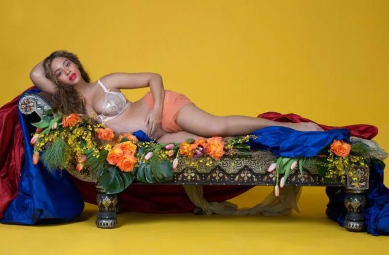 Η Beyoncé σε φωτογράφιση εγκυμοσύνης ξαπλωμένη σε ανθοστόλιστο ανάκλιντρο.