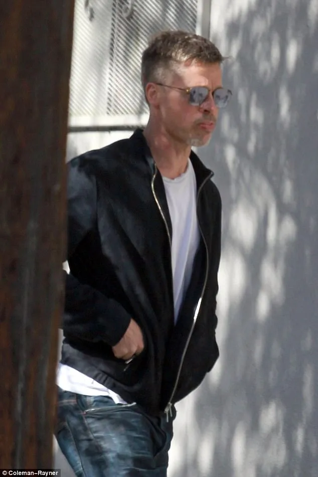 Ο Brad Pitt με μαύρο τζάκετ, γυαλιά ηλίου και τζιν παντελόνι περπατά στο δρόμο.