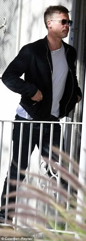 Ο Brad Pitt με μαύρο τζάκετ και γυαλιά ηλίου έξω από κτίριο.