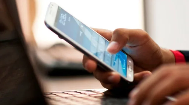 Κοντινό πλάνο χεριών που χρησιμοποιούν smartphone πάνω από πληκτρολόγιο laptop.