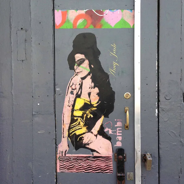 Street art γκράφιτι της Amy Winehouse σε γκρίζα πόρτα.
