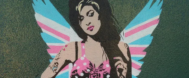 Γκράφιτι της Amy Winehouse με φτερά αγγέλου σε πράσινο τοίχο.