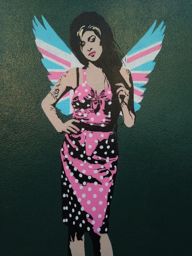 Stencil graffiti της Amy Winehouse με φτερά αγγέλου σε πράσινο τοίχο.