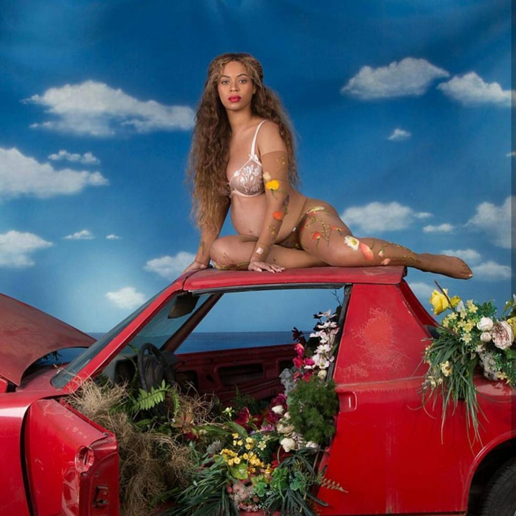Η Beyoncé έγκυος ποζάρει πάνω σε ένα κόκκινο αυτοκίνητο γεμάτο λουλούδια.