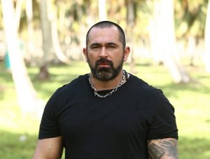 Άνδρας με μαύρο t-shirt και αλυσίδα στο λαιμό σε εξωτερικό χώρο.