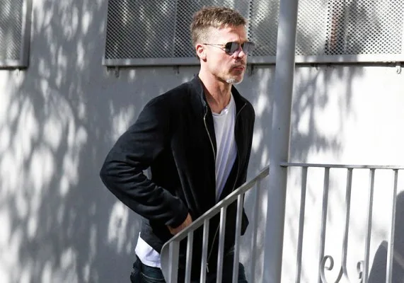 Ο Brad Pitt με μαύρο τζάκετ, λευκό t-shirt και γυαλιά ηλίου σε εξωτερικό χώρο.