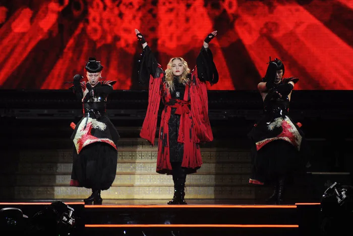 Η Madonna στη σκηνή με δύο χορευτές, φορώντας κόκκινο και μαύρο ένδυμα.