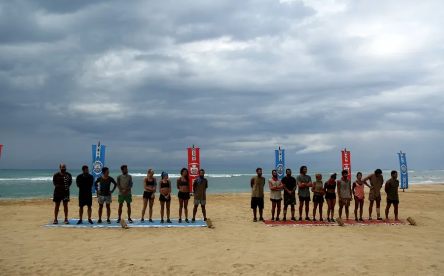 Παίκτες του Survivor σε παραλία μπροστά από σημαίες των ομάδων τους.