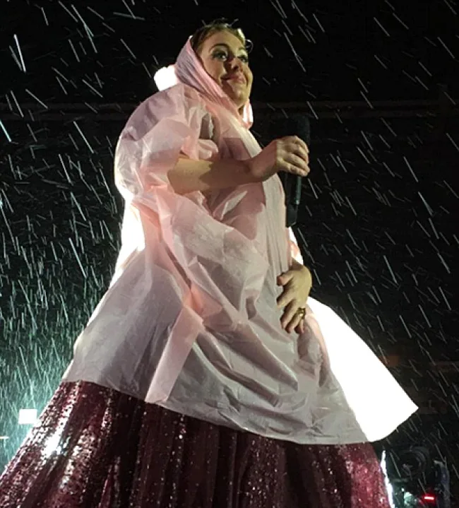 Η Adele στη σκηνή φορώντας ροζ αδιάβροχο κάτω από τη βροχή.