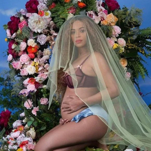 Η Beyoncé ποζάρει έγκυος μπροστά από μια σύνθεση με λουλούδια.