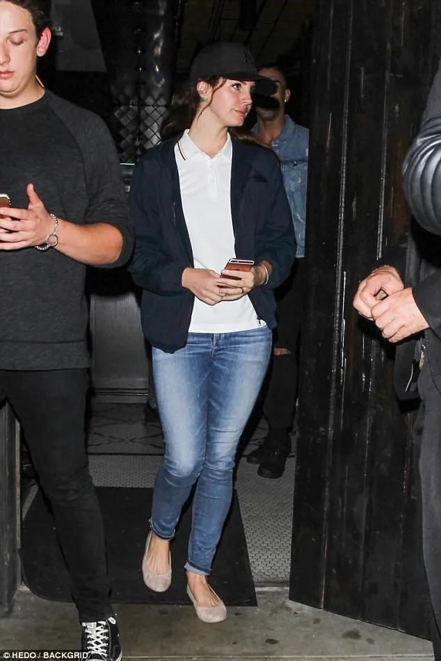 Η Lana Del Rey με casual εμφάνιση, φορώντας καπέλο και τζιν, κρατώντας το κινητό της.