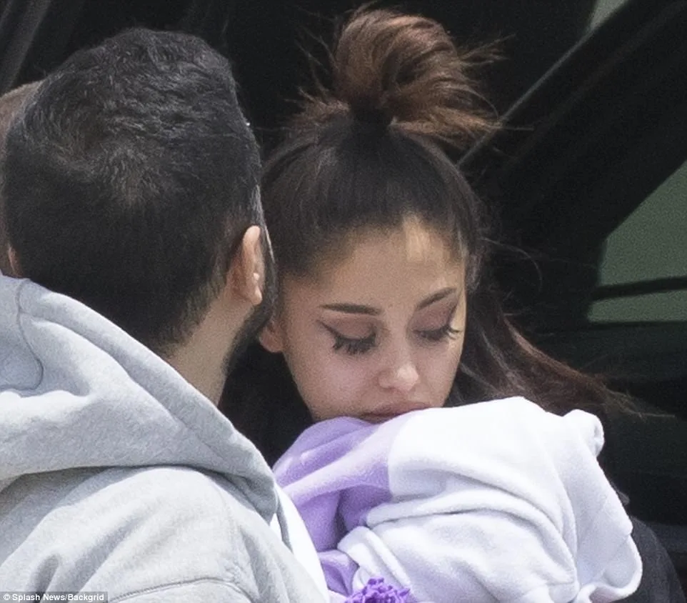 Η Ariana Grande με σκυμμένο κεφάλι και πιασμένα μαλλιά δίπλα σε έναν άνδρα.