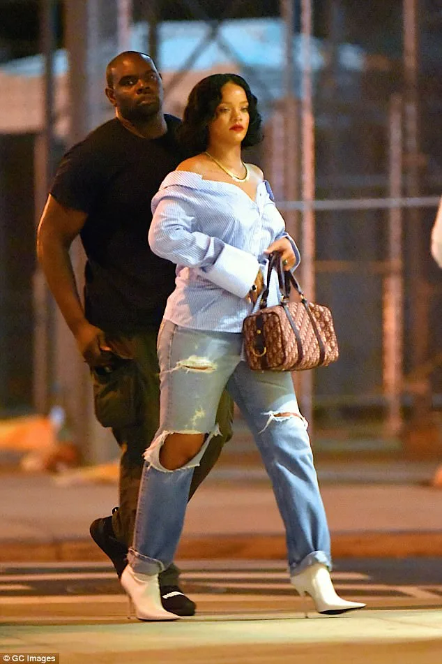 Η Rihanna περπατά στο δρόμο με ριγέ πουκάμισο και σκισμένο τζιν.
