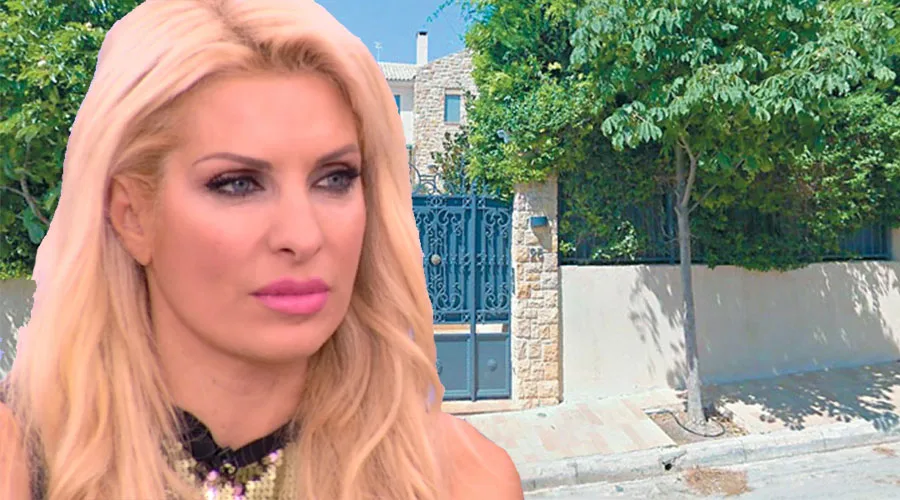 Η Ελένη Μενεγάκη σε κοντινό πλάνο με φόντο ένα πέτρινο σπίτι.