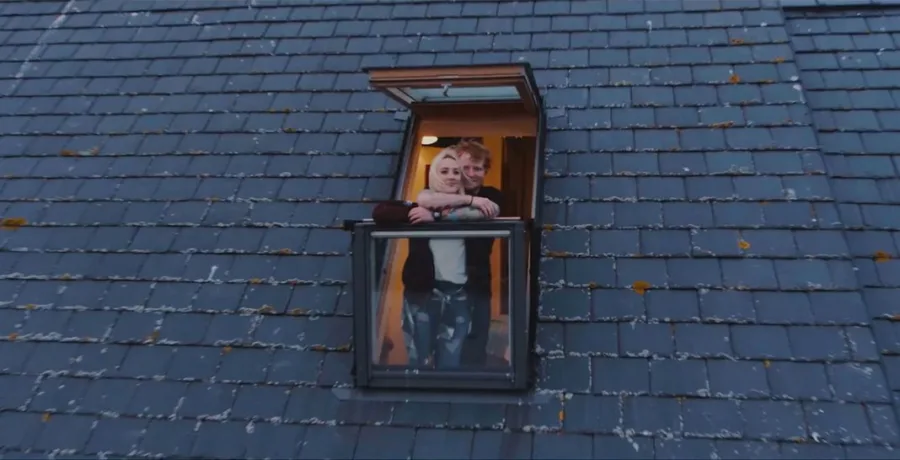Ο Ed Sheeran αγκαλιάζει μια γυναίκα σε ένα παράθυρο στέγης.