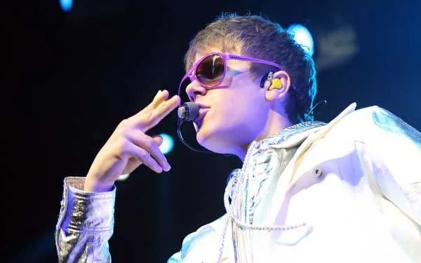 Ο Justin Bieber σε συναυλία με μοβ γυαλιά ηλίου και λευκό τζάκετ.