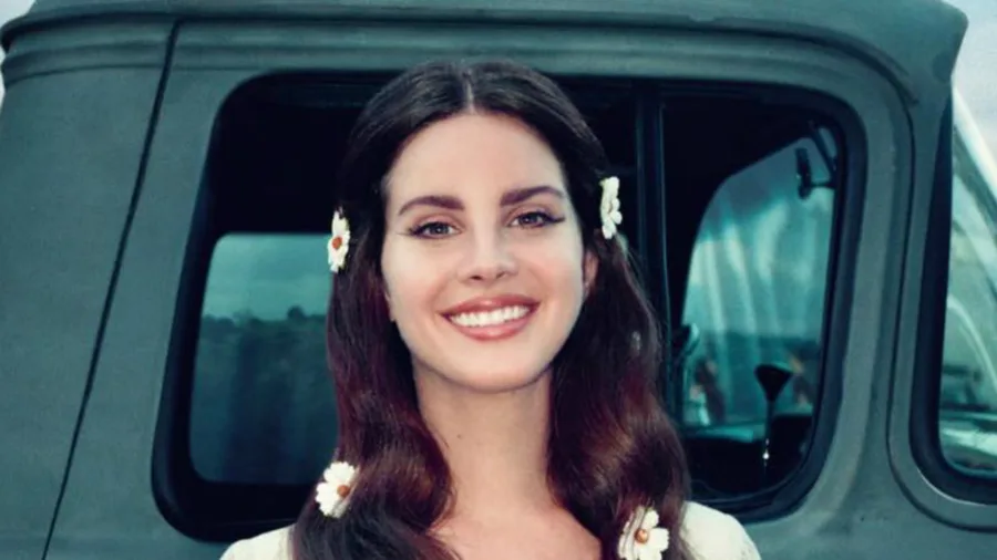 Η Lana Del Rey με λουλούδια στα μαλλιά μπροστά από ένα όχημα.